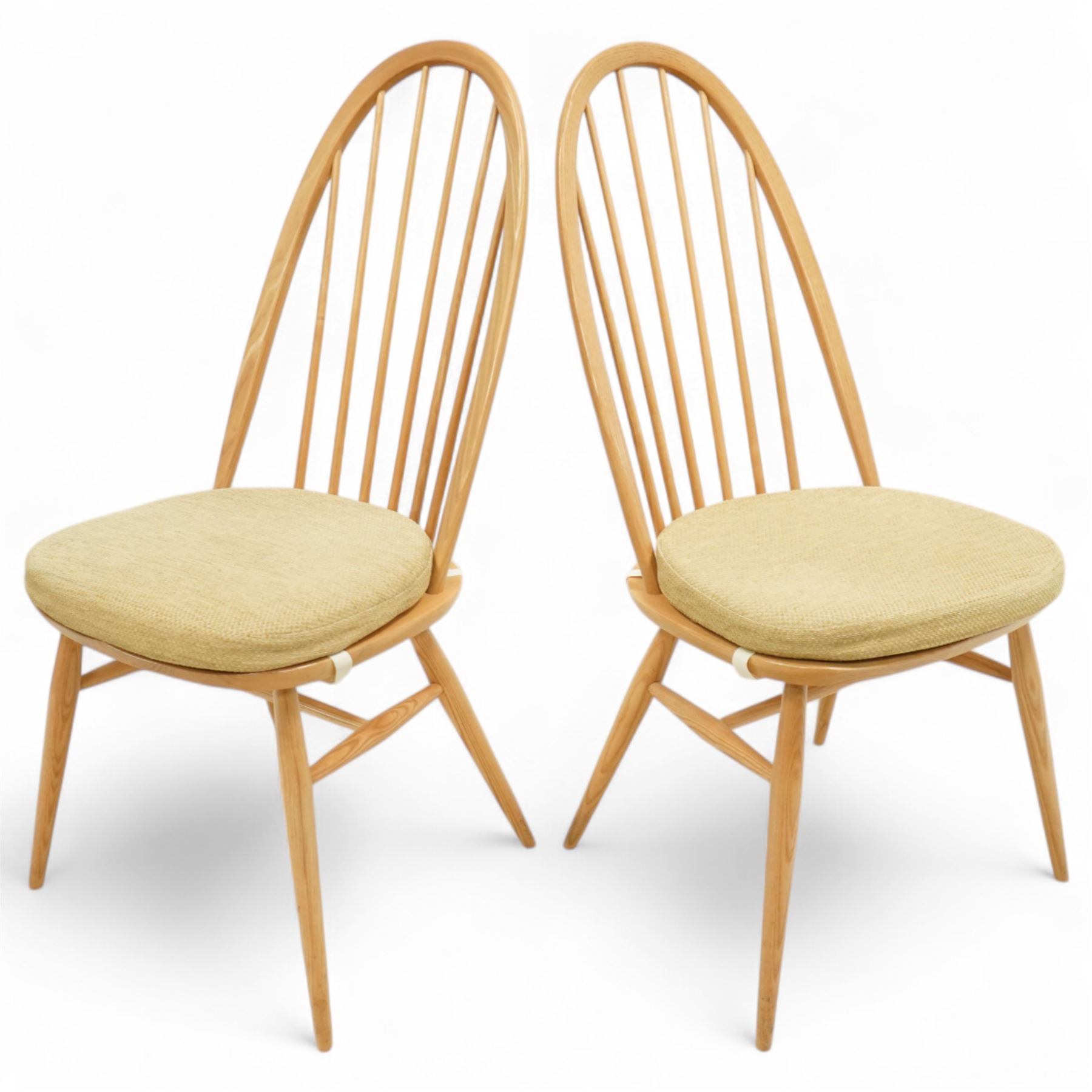 Ercol - light elm set of four Quaker style chairs, high arched backrest with slender spindles, solid wood seat with elasticated strap cushion, on round tapered out swept legs (4)
