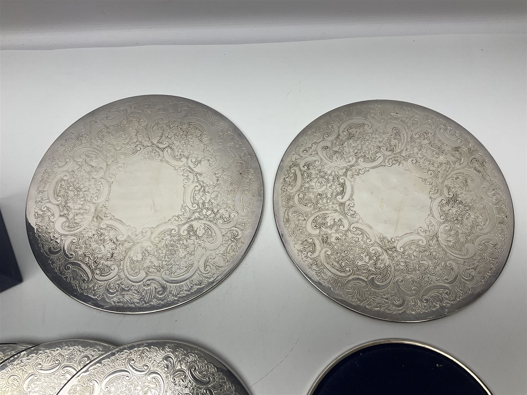 Set of eight silver plated placemats, each of circular form with engraved scroll and floral decoration, including two larger and six smaller examples, largest D23cm, in fitted case 