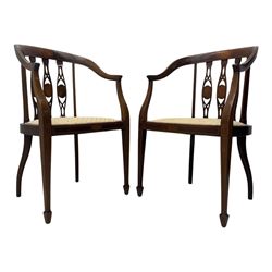 Pair of Edwardian mahogany tub chairs, curved top rail inlaid with oval marquetry panels, the backs with a pierced, elongated splat design featuring a central oval motif, the seats upholstered in cream fabric, on square tapering supports with spade feet