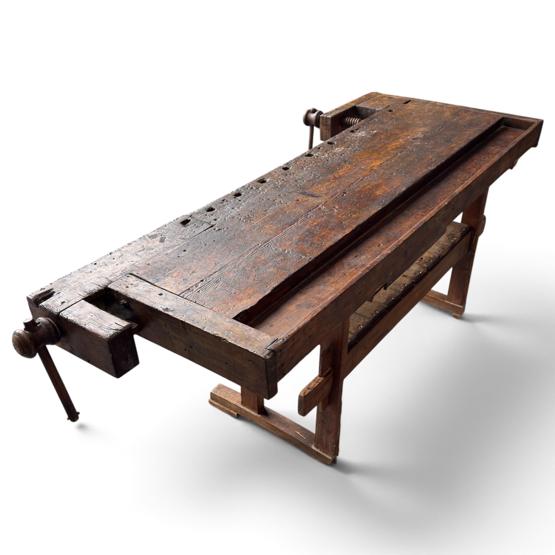 Large early 20th century rustic stained reclaimed pine workbench, the substantial plank top with recessed tool well and two homemade wooden screw vices, above a single frieze drawer and slatted undertier, raised on trestle end supports