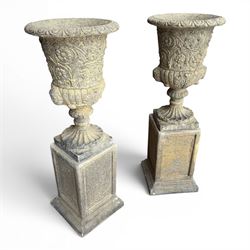 Pair of George III design antiqued composite stone garden urns of campana form, the egg-and-dart everted rim over a waisted body relief moulded with scrolling fruiting foliage and flowerheads, the gadrooned underbelly with twin mask ornaments, the knopped stems on fluted socles, raised on faux panelled square pedestal bases