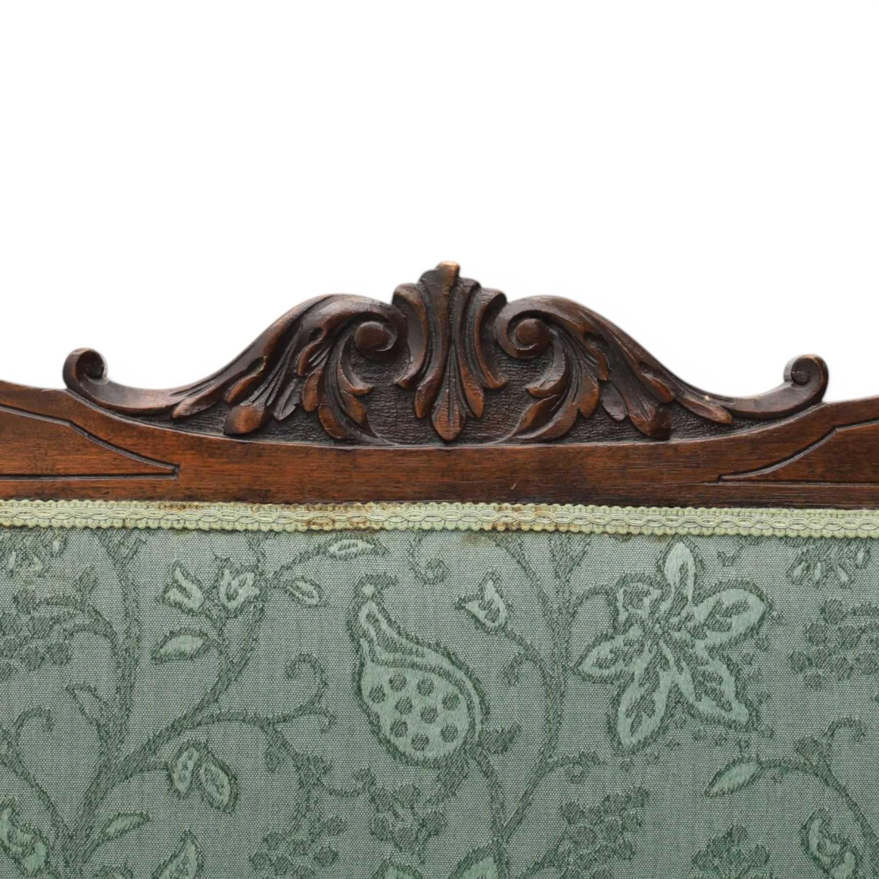 Edwardian mahogany framed sofa, shaped cresting rail with scroll terminals and carved foliate pediment, upholstered back and swept arms in green foliate fabric, pierced splat supports, serpentine front seat rail, on cabriole supports terminating in castors