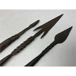 Native hand forged iron fishing spear, the V-shaped head with barbed neck and hewn haft L171cm; and two other hand forged iron spear heads, one with remains of copper bound haft (3)
