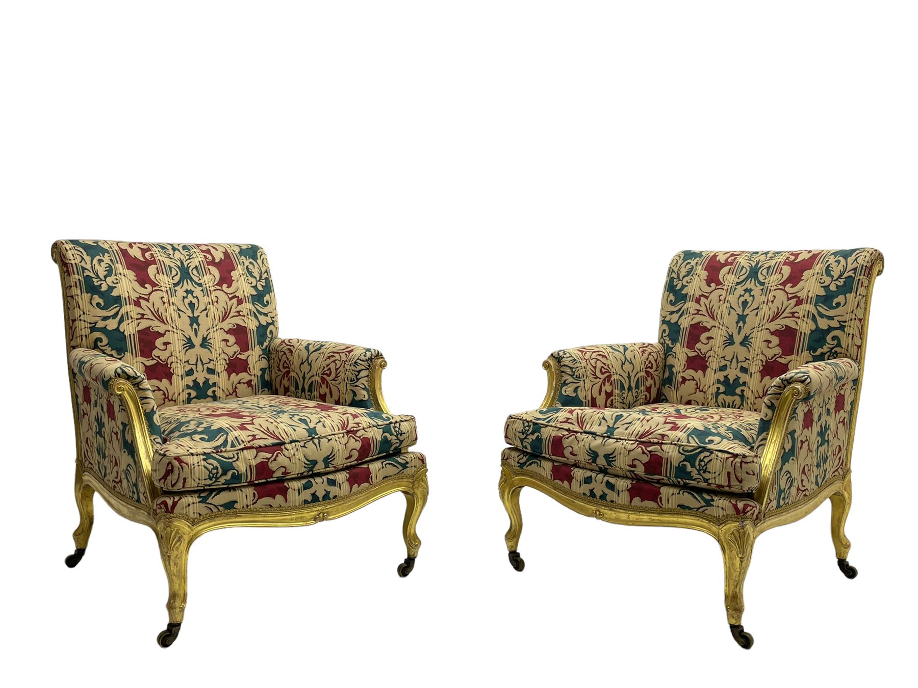 William Bertram & Son of London - pair late 19th century giltwood armchairs, moulded frame with scroll carved back and arm terminals, upholstered in striped fabric with foliate pattern, on shell carved cabriole supports, the brass castors stamped 