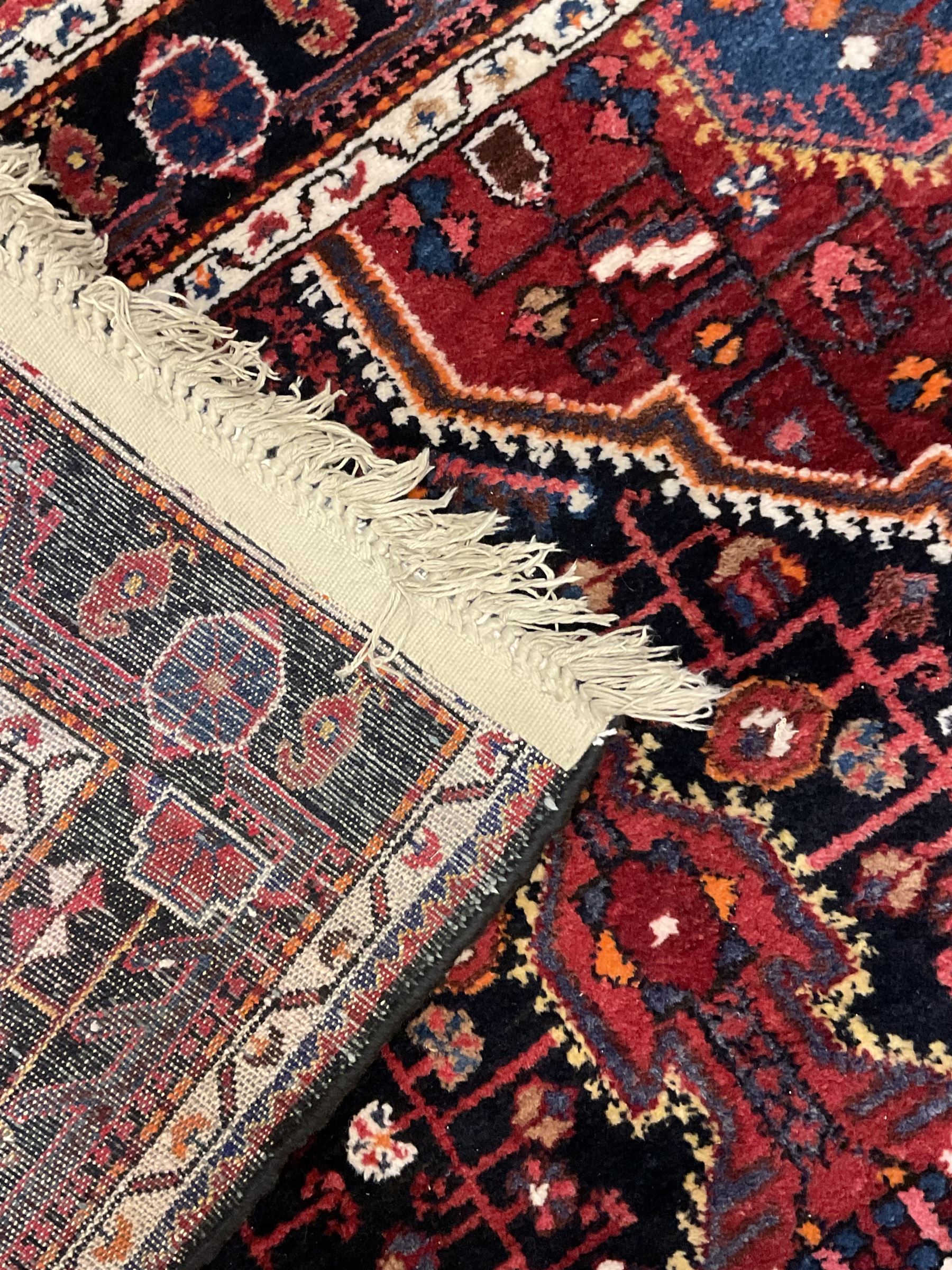 Persian Hamadan red and indigo ground rug, central lozenge medallion with extending poles, the field decorated with interlaced branches and flowerheads, guarded border with stylised floral motifs