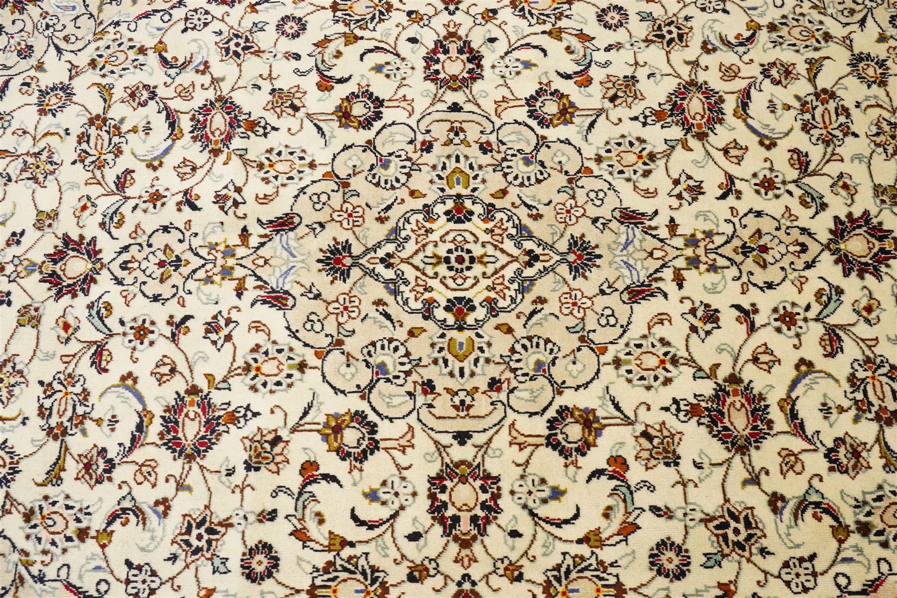Central Persian Kashan hand-knotted carpet, ivory field with central lobed medallion issuing an all-over design of scrolling vines, palmettes, and floral sprays, within conforming spandrels, enclosed by a foliate border, framed by multiped guard stripes, with cotton fringe ends 