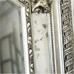 Impressive Baroque Revival mirror in antique silvered finish, the pierced cartouche shell pediment flanked  by C-scrolls and flower heads, the outer frame with ribbon-twist motifs throughout, the central arched bevelled plate surrounded by further rectangular mirror panels with cartouche mounts