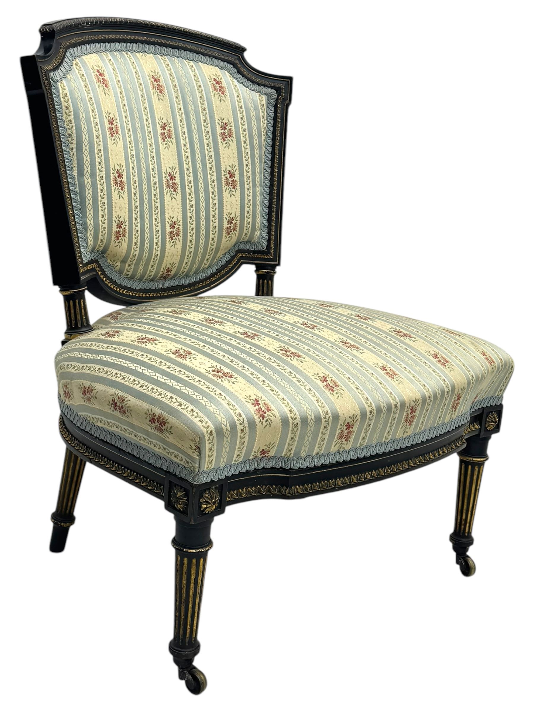 19th century French ebonised low chair, upholstered in floral striped fabric within a moulded frame with gilt line and foliate decoration, the seat of serpentine form, raised on turned fluted legs with toupie feet