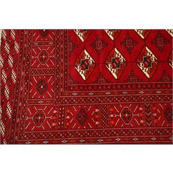 Turkmen hand-knotted carpet, deep crimson ground field, with an all-over lattice of repeating diamond guls, each enclosing angular cruiform motifs, and stylized tribal devices, interspersed with smaller geometric ornaments, main border decorated with repeating geometric motifs and stylized tribal elements, flanked by narrow guard stripes, with cotton fringe ends 
