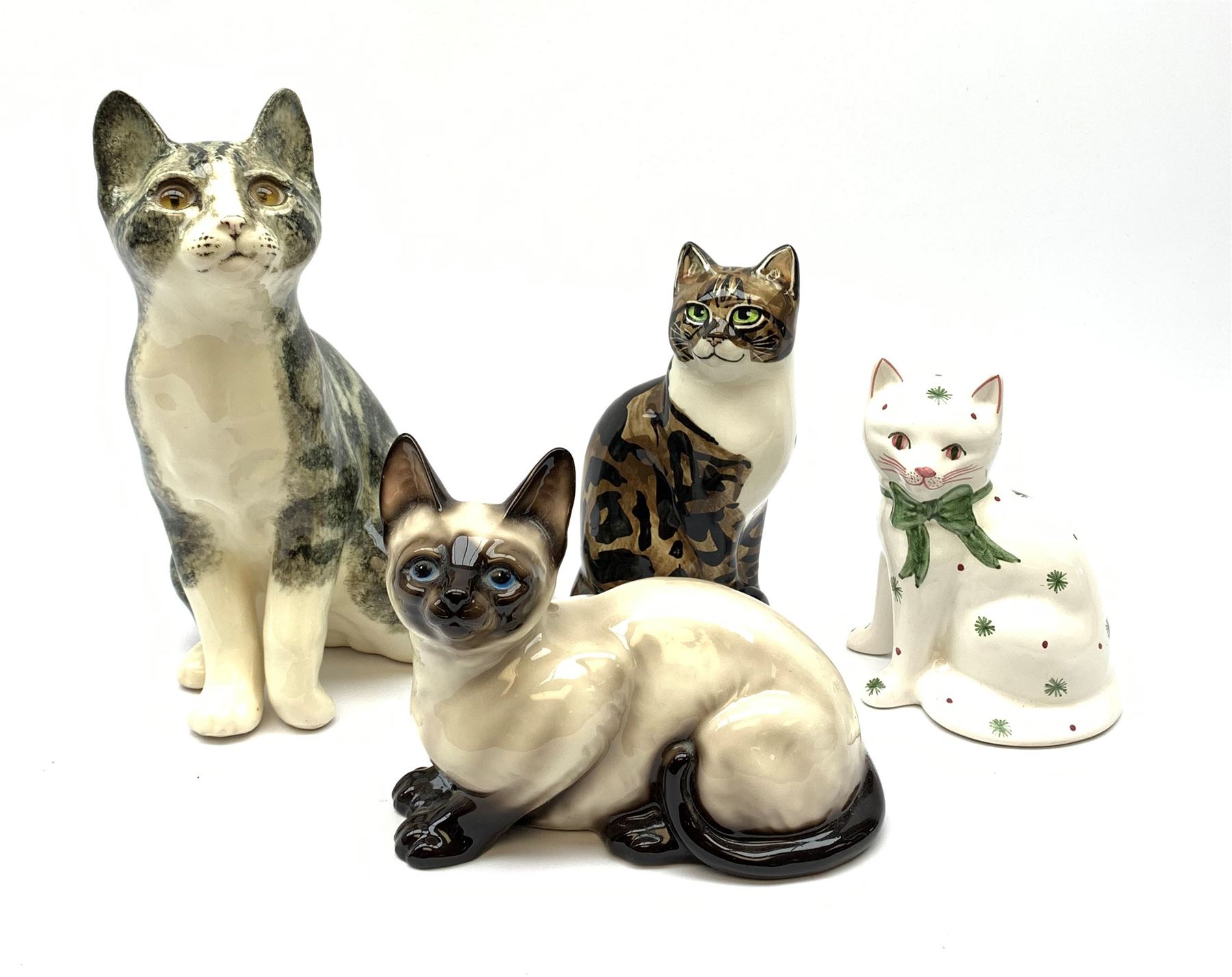 A Winstanley cat, with glass eyes in seated post, signed beneath, H25cm, together with three other figures of cats, including a Rye Pottery example. (4). 