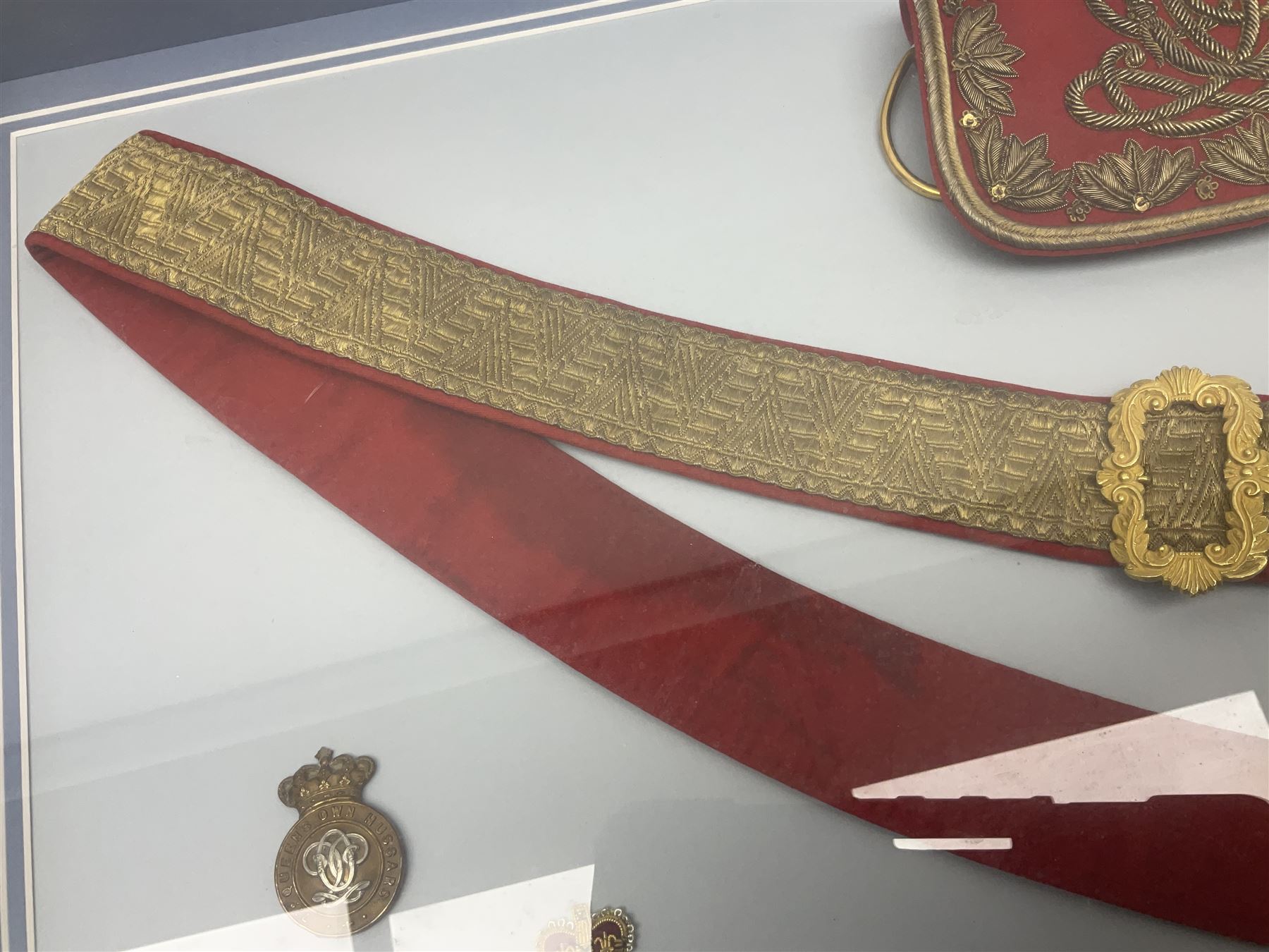 Victorian / Edward VII Queens Own Hussars Officers Full Dress Pouch and Cross Belt; scarlet cloth covered leather pouch with bullion embroidered crown, laurel bordered regimental crest within an edge of embroidered bullion wire; with its original officers cross belt with fine regimental pattern brocade to the top and gilt metal furniture; displayed in a wall hanging case with cloth and metal regimental badges; mahogany stained frame 44 x 54cm