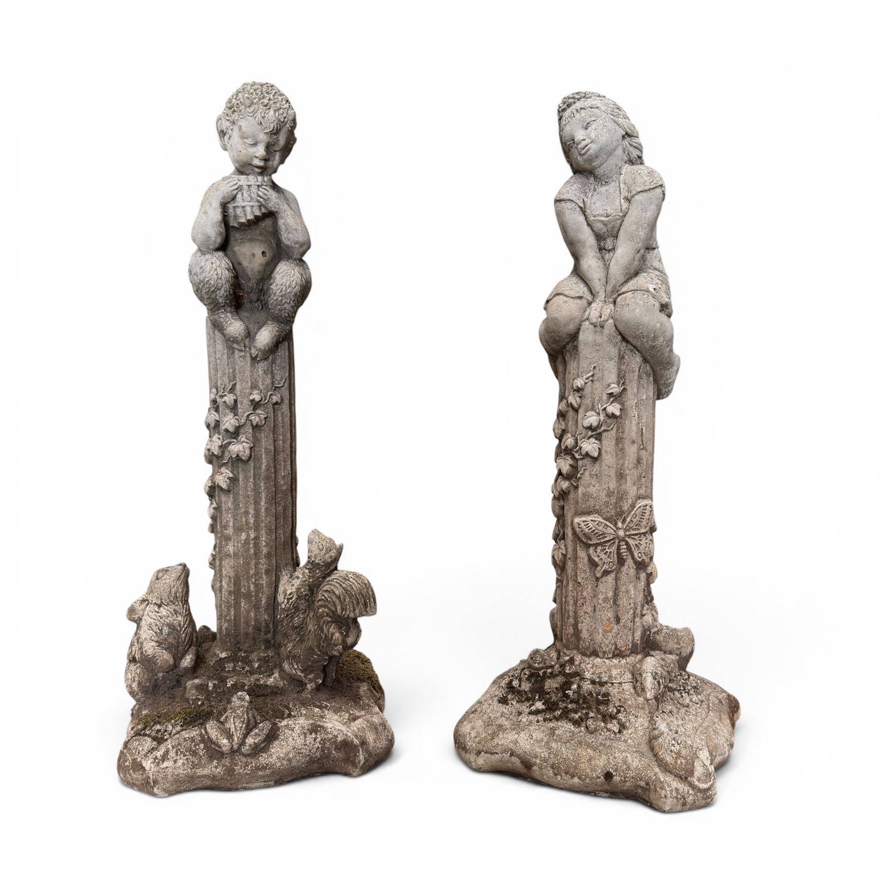 Pair of weathered composite stone garden figures, modelled as a girl and a young satyr playing the panpipes seated on column supports, the fluted columns with climbing ivy vines and surmounted animal, butterfly and other zoomorphic motifs