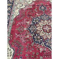 Large Persian carpet, the red ground field decorated with large rosette medallion, trailing foliate design decorated with stylised plant motifs, pale ground spandrels decorated with scrolls, repeating stylised flower head border with guards 