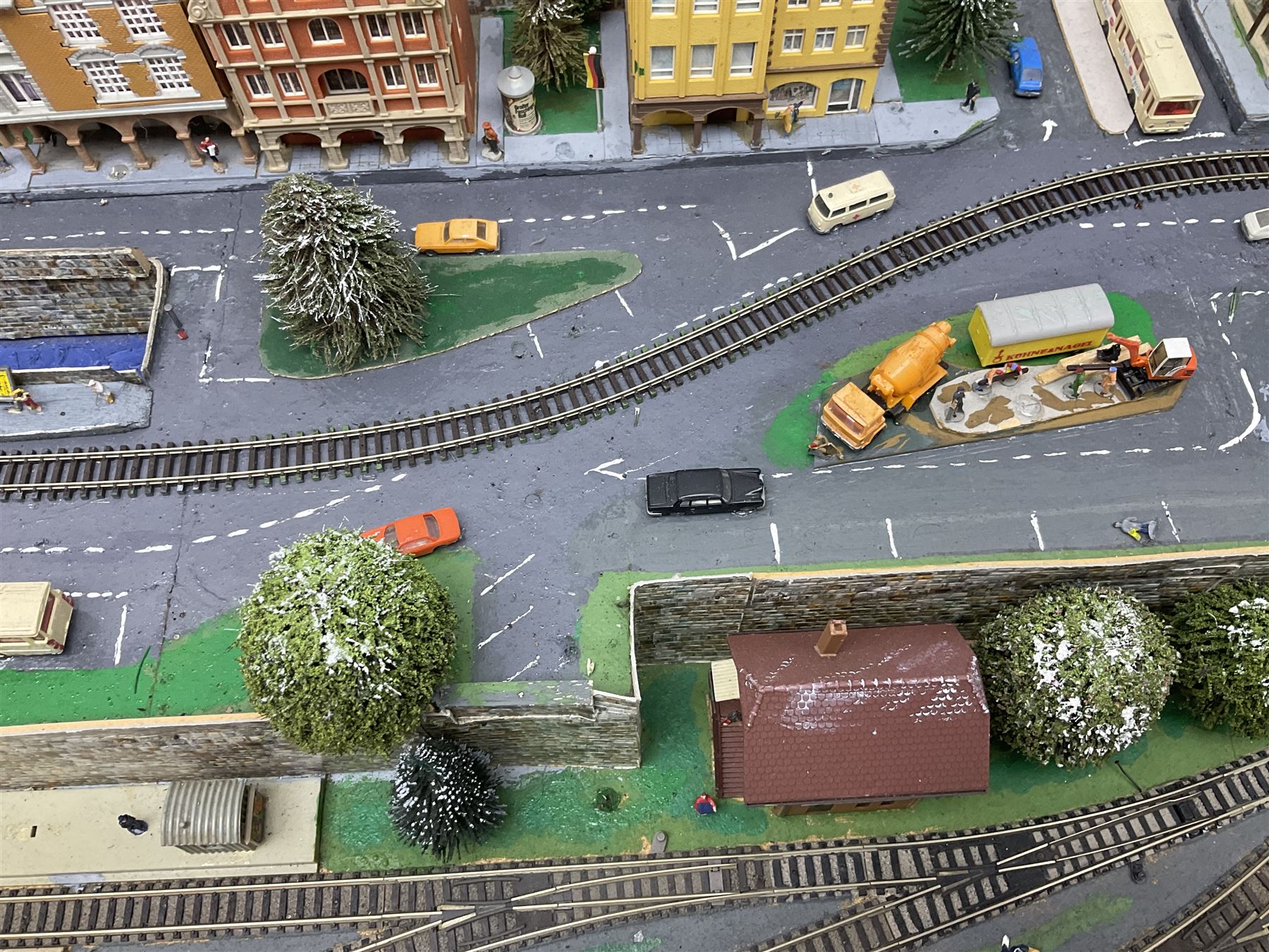 Table top 'N' gauge continental scenic layout as a split level town with various loops of track, station with numerous platforms, engine shed, assorted buildings, roads with motor vehicles and figures, tunnels, trees, river with bridge, tram depot etc 122 x 52cm