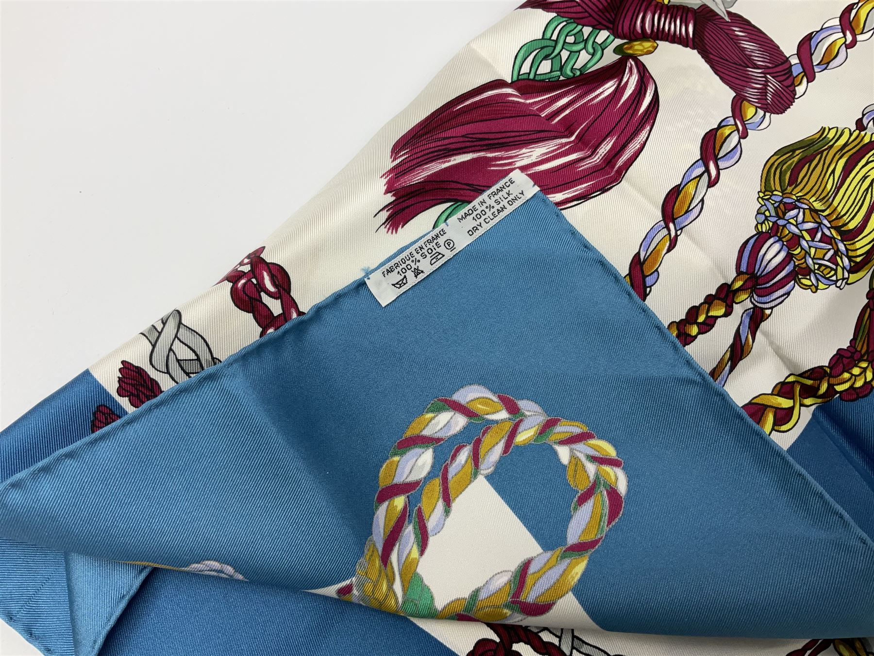 Hermès 'Le Timbalier' silk scarf, designed by Francoise Heron in 1961, printed with a central image of a gentleman on horseback donning extravagant dress, on white ground surrounded with colourful stylised knotted ropes, contained within peacock blue border, with rolled hand stitched edges and Hermes material label, 87cm square