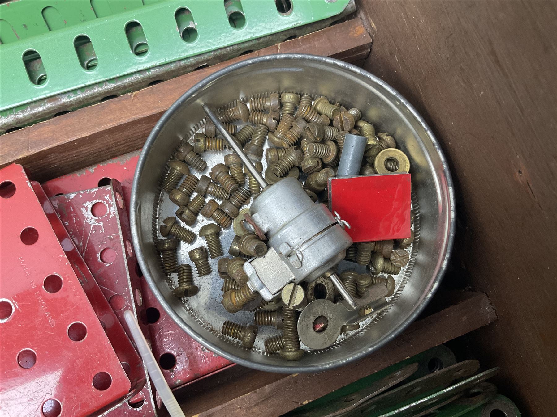 Meccano - large quantity of loose parts including various plates and strips, flanged plates, pulleys, axle rods and crank handles, wheels and tyres, gear wheels, brackets, nuts & bolts, various manuals; predominantly red and green; some in compartmentalised wooden trays