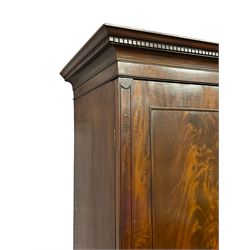 George III mahogany double wardrobe, the projecting cornice with dentil moulding over two panelled doors with mirror-lined interiors, enclosing hanging rails and brass hooks, the base fitted with two drawers, raised on bracket feet