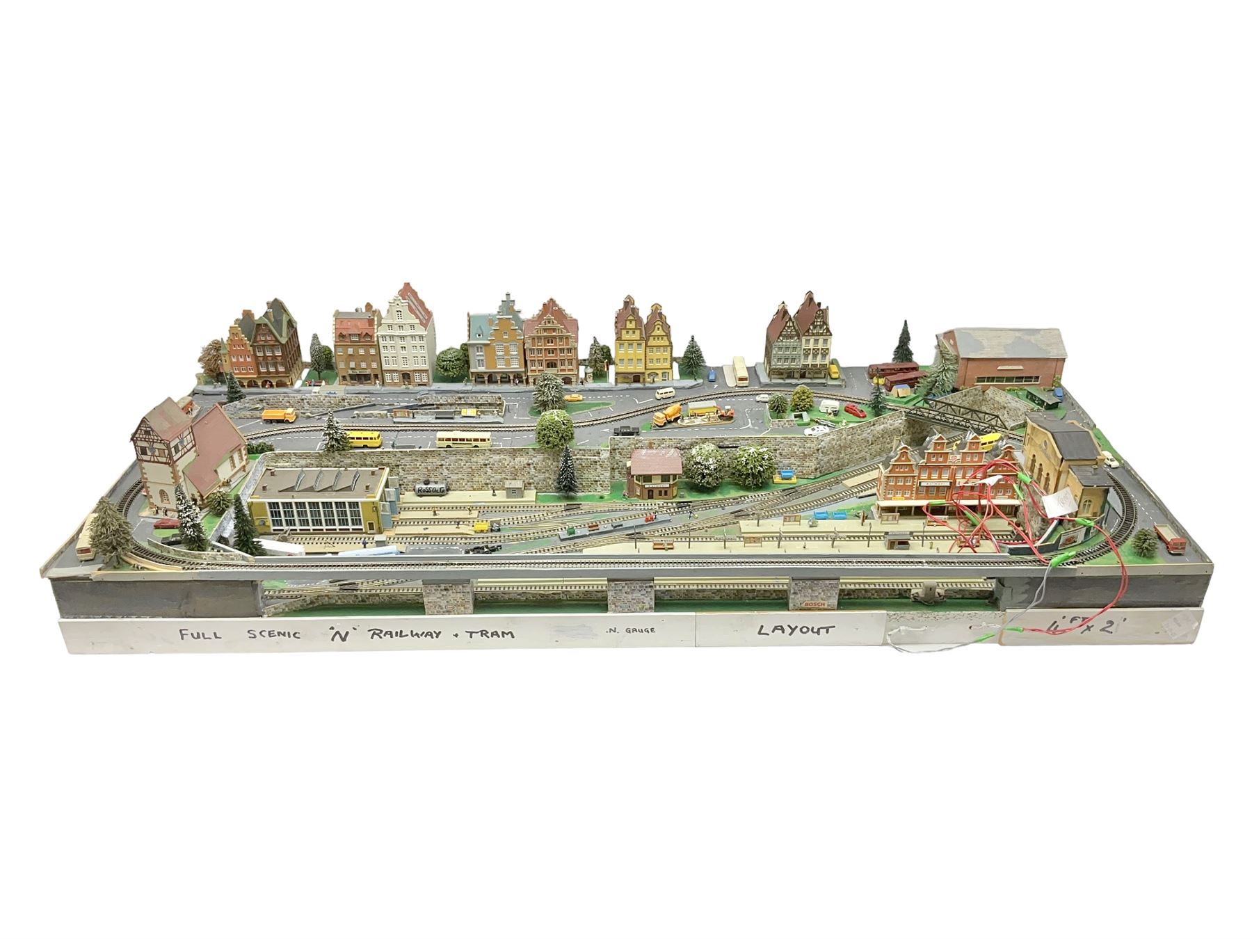 Table top 'N' gauge continental scenic layout as a split level town with various loops of track, station with numerous platforms, engine shed, assorted buildings, roads with motor vehicles and figures, tunnels, trees, river with bridge, tram depot etc 122 x 52cm