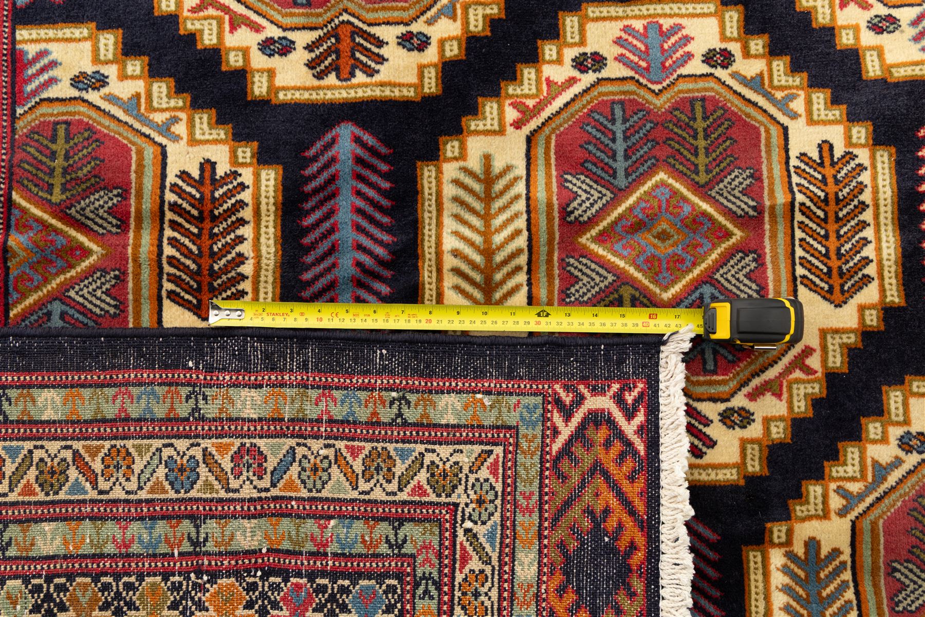 Central Asian Turkmen, main field with octagonal guls enclosing hooked diamond motifs in shades of madder gold, ivory, and indigo set against a dark ground within multiple polychrome borders of geometric devices and stepped motifs 