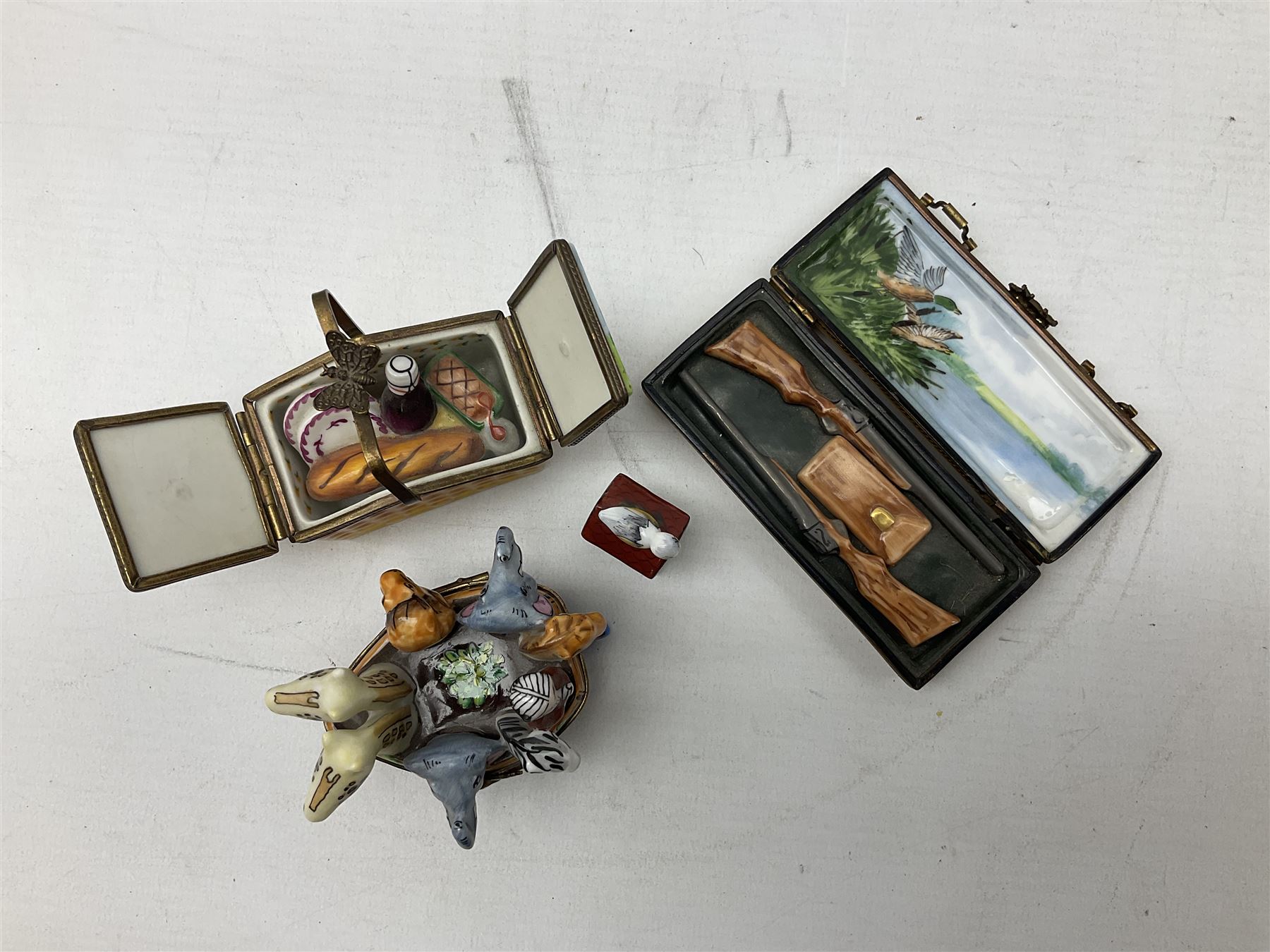 Group of Limoges trinket boxes, to include a number of novelty examples, including examples modelled as Noah's ark, shotgun case containing shotguns, picnic basket containing food, toad reading book seated upon a lily pad, etc., (9)