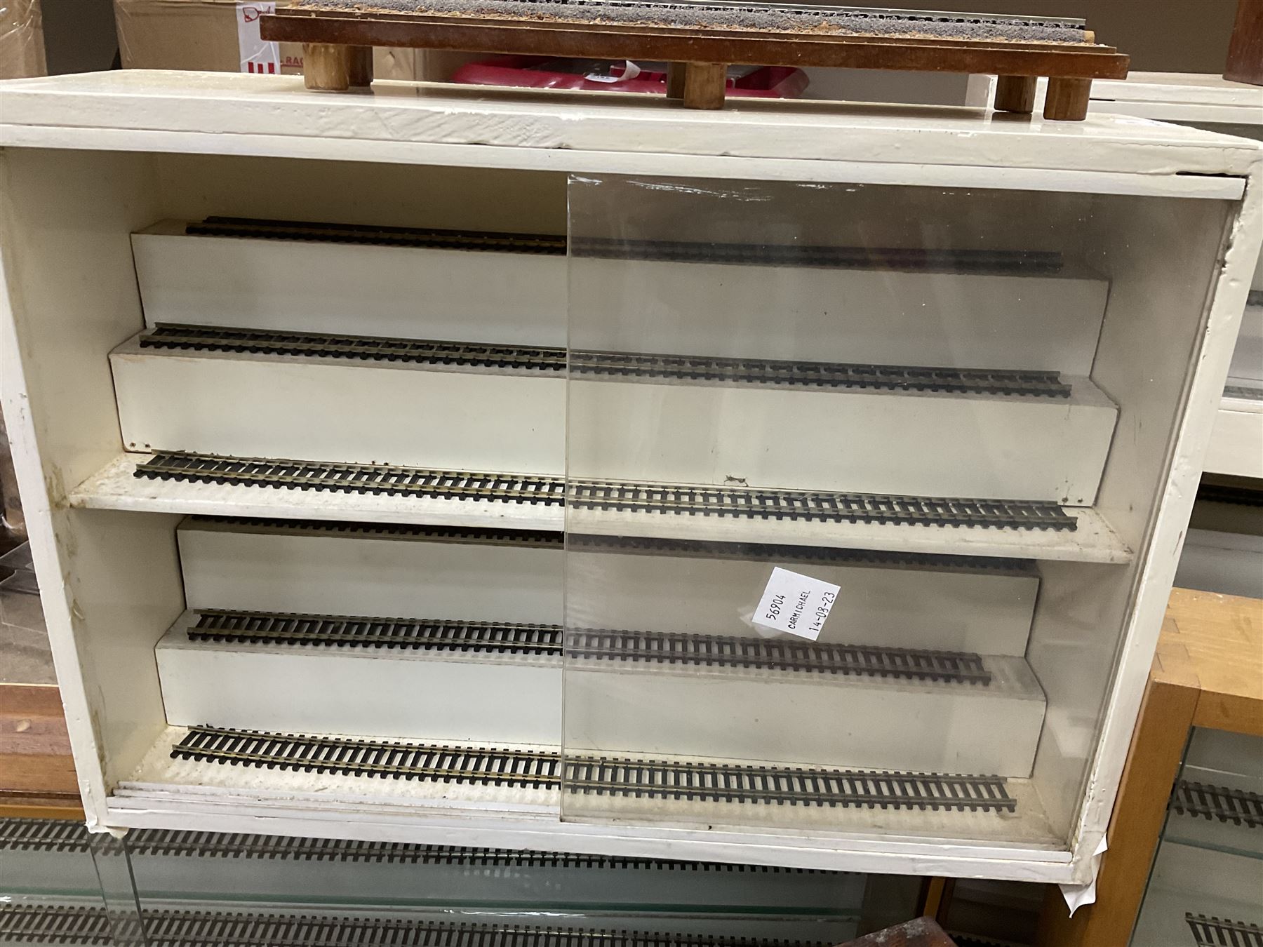 Six shelved cabinets for displaying ‘00’ gauge locomotives comprising plain plywood and white painted examples with track applied to various shelves, largest H63cm, W107cm, D27cm; Collection of tools for building model locomotives to include Weller PU-2D Soldering Pencil and Standard Tip Soldering Iron 20W/230V, Humbrol Modellers Airbrush, Power Supply Units and two wooden chests one of which housing a collection of tools including tweezers, scalping tools, wrenches etc 