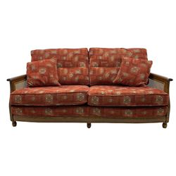 Ercol medium elm framed three seat bergere sofa, and pair of matching armchairs upholstered in red fabric