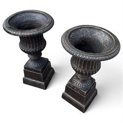 Pair of Neoclassical design black and gilt painted cast iron garden urns of campana form, with egg-and-dart rims and fluted bodies, on knopped stems, fluted socles and stepped square plinth bases