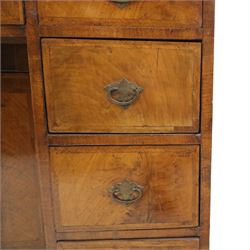 Early 20th-century Georgian-style walnut kneehole desk, the rectangular top with feather cross-banded border, above an arrangement of eight short drawers flanking a central cupboard door, fitted with brass backplate handles, raised on bracket feet