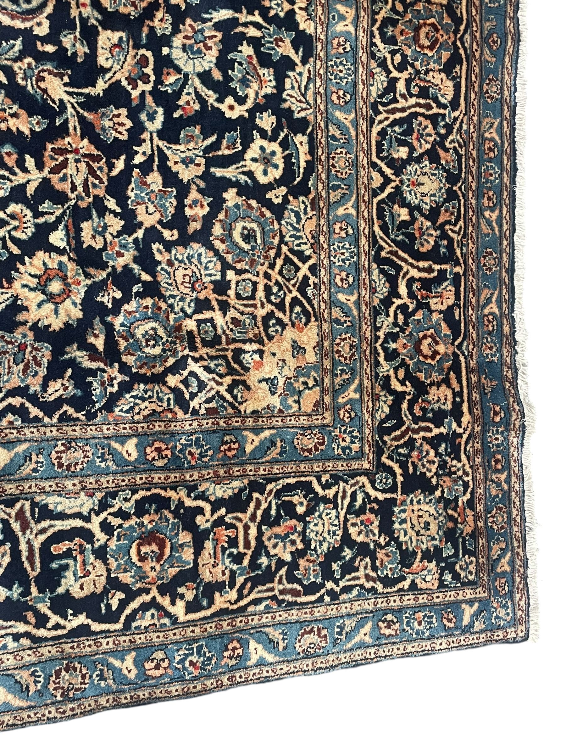 Persian Kashan indigo ground rug, the rosette medallion decorated with projecting palmettes, on a field of swirling leafy branches and decorated with further palmettes, the scrolling border with repeating stylised plant motifs, within floral pattern guard stripes