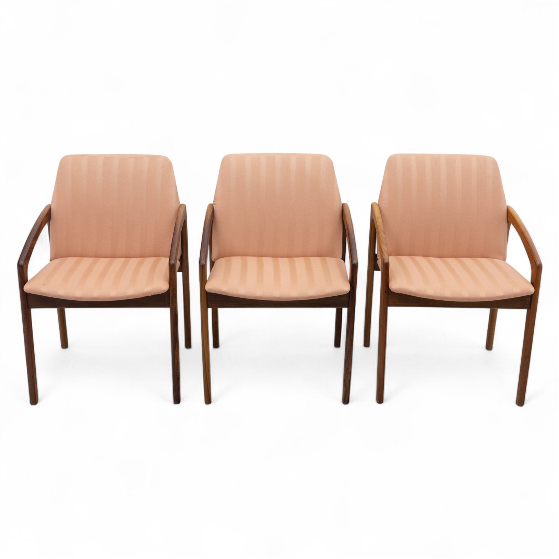 Mid-20th century Danish teak armchairs, each with curved open arms and upholstered seat and backrest in salmon pink striped fabric, raised on tapering legs