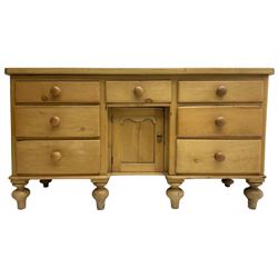 Late 19th century pine sideboard or dresser base, central drawer over recessed cupboard, flanked by six graduating drawers, raised on turned feet