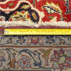 Central Persian Kashan hand-knotted carpet, crimson ground, with a large central ivory and dark navy floral medallion with pendants, surrounded by dense scrolling foliate and floral motifs incorporating rosettes, palmettes and vine work, enclosed by ivory spandrels and a dark navy border with repeating palmettes and meandering vines, flanked by floral guard stripes