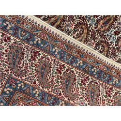 Persian Kirman carpet, the ivory ground field and border decorated with repeating Boteh motifs, interspaced with all-over floral design, blue ground border guards, the top border with signature panel