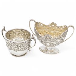 Late Victorian silver twin handled sugar bowl, profusely embossed with floral and scrolling decoration and acanthus capped handles, upon stepped oval base, hallmarked Josiah Williams & Co, London 1897, together with a Victorian twin handled sugar bowl, of circular form with embossed and chased foliate decoration and seated figures capping each handle, upon circular base, hallmarked London 1888, maker's mark indistinct, tallest H11cm
