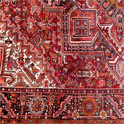 North West Persian Heriz hand-knotted carpet, brick red field, with large central angular star medallion with stepped outlines, surrounded by geometric floral devices and stylized rosettes, with corresponding corner spandrels, enclosed by a bold geometric main border with multiple guard stripes, with cotton fringe ends 