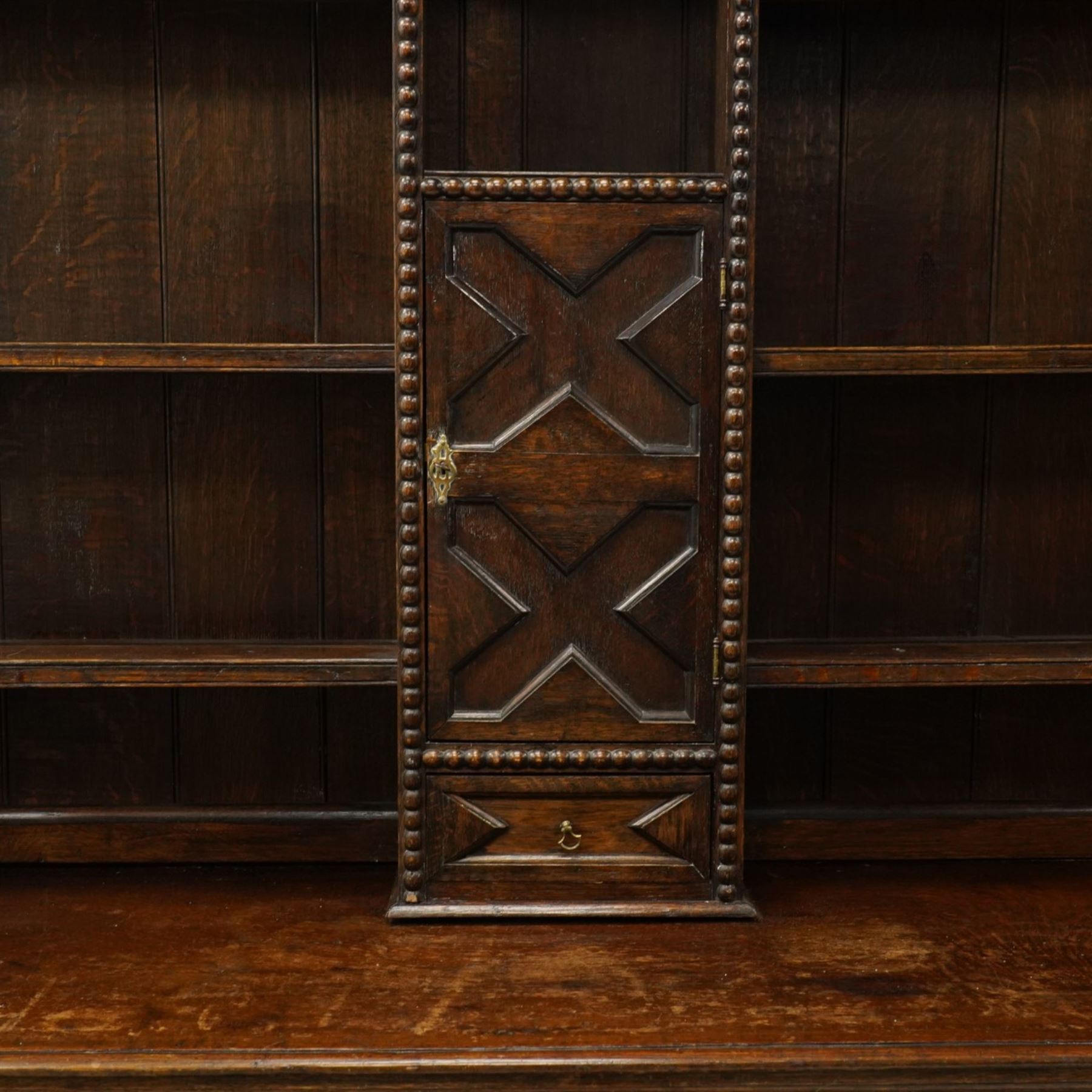 19th century Jacobean Revival oak dresser and rack, the upper section with open shelves and central cupboard, flanked by bobbin moulded uprights, the base fitted with three carved drawers with brass ring handles, raised on turned supports united by stretchers