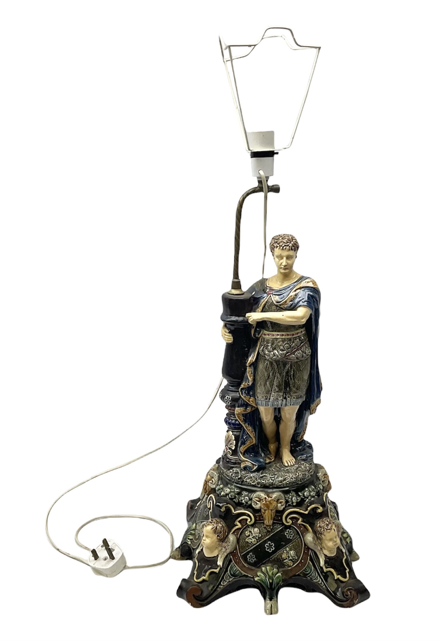 Composite table lamp modelled as a Roman Emperor donning blue robes, upon quatrefoil base modelled with rams heads and winged cherubs, H56cm excl fitting