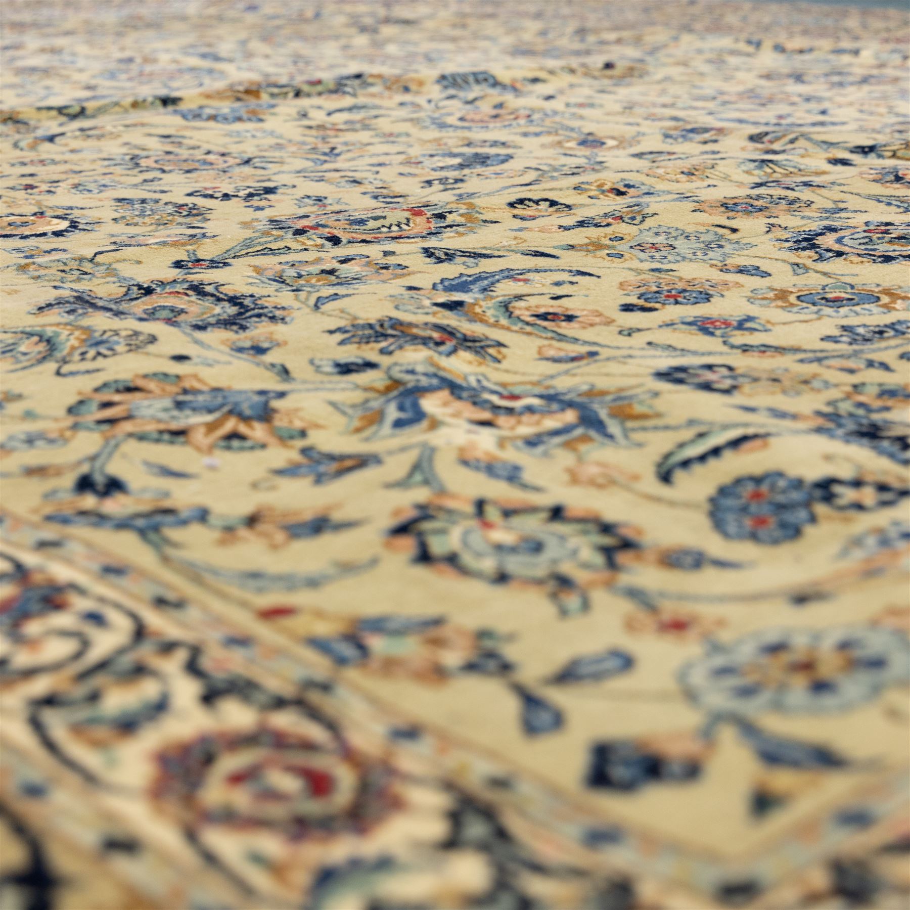 Persian Kashan carpet, beige ground, field with an all-over design of scrolling palmettes and floral sprays in blue and terracotta within a ivory ground and pale blue floral border