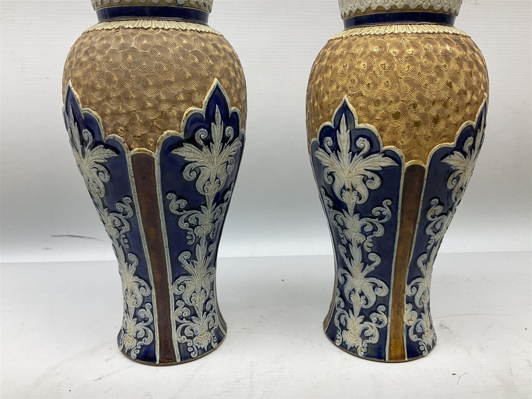 Pair of Royal Doulton Lambeth stoneware baluster vases, decorated in light relief with panels of foliage on blue ground, with gilt scrolls above, impressed mark beneath, 28cm high