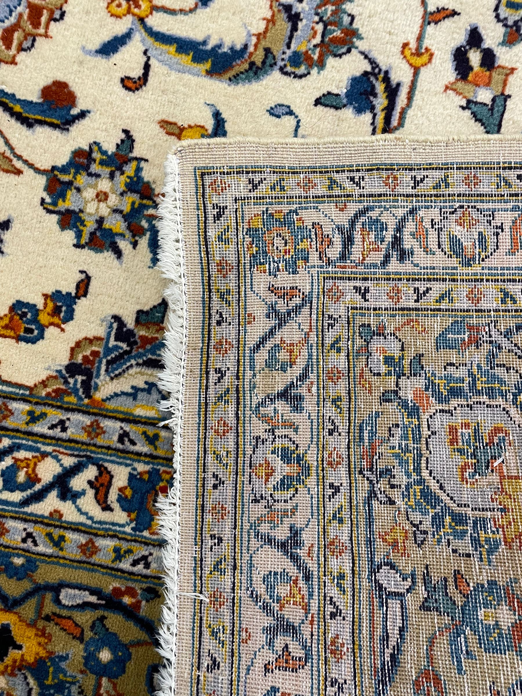 Persian Kashan ivory ground carpet, the field decorated with trailing foliate branches and stylised flower head motifs, guarded border with repeating design decorated with scrolling leafy branch and plant motifs 