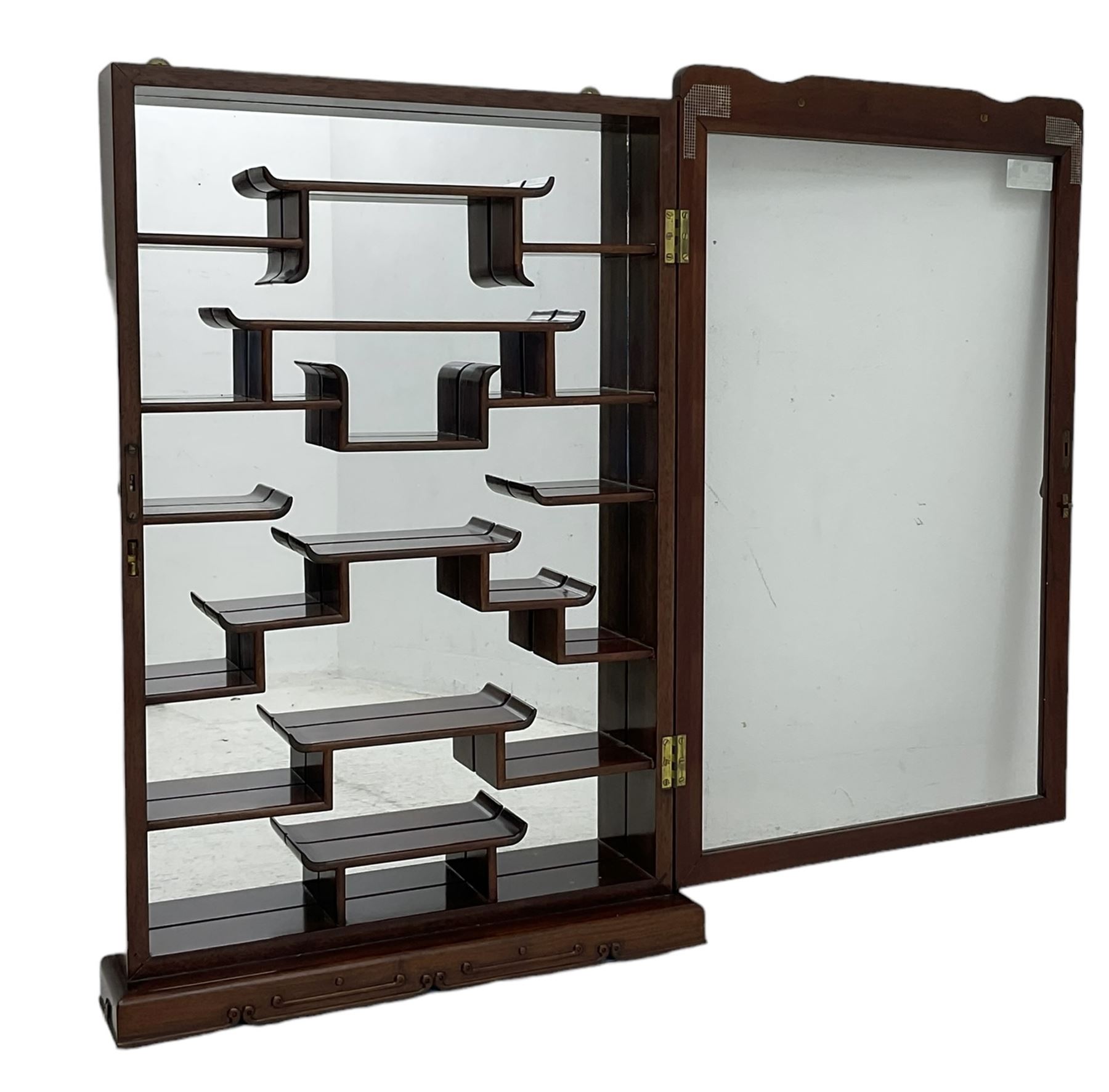 Chinese hardwood wall hanging curio cabinet, the mirror interior fitted with stepped shelves, enclosed by single glazed doors, decorated with carved scrolling foliage 
