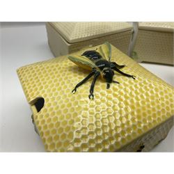 Four square honey boxes with lids,  each decorated with honeycomb pattern and finished with a bee finial
