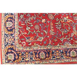 Persian Kashan crimson ground rug decorated with scrolling foliage, the indigo guard stripes with repeating stylised palmette motifs