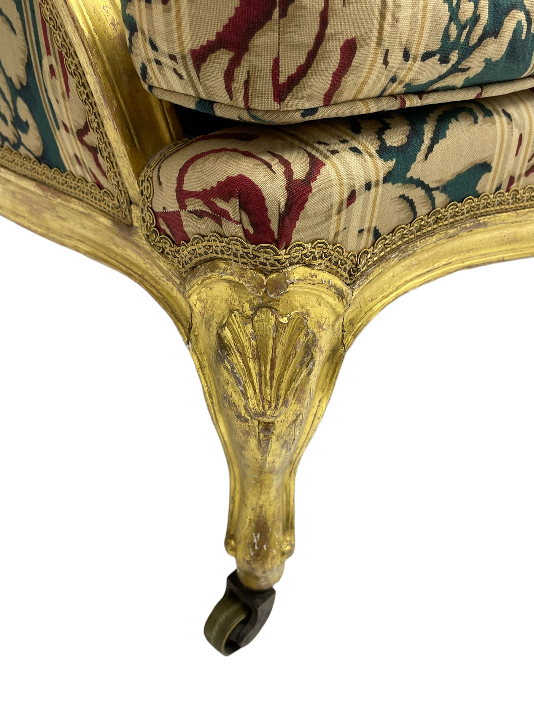 William Bertram & Son of London - pair late 19th century giltwood armchairs, moulded frame with scroll carved back and arm terminals, upholstered in striped fabric with foliate pattern, on shell carved cabriole supports, the brass castors stamped 