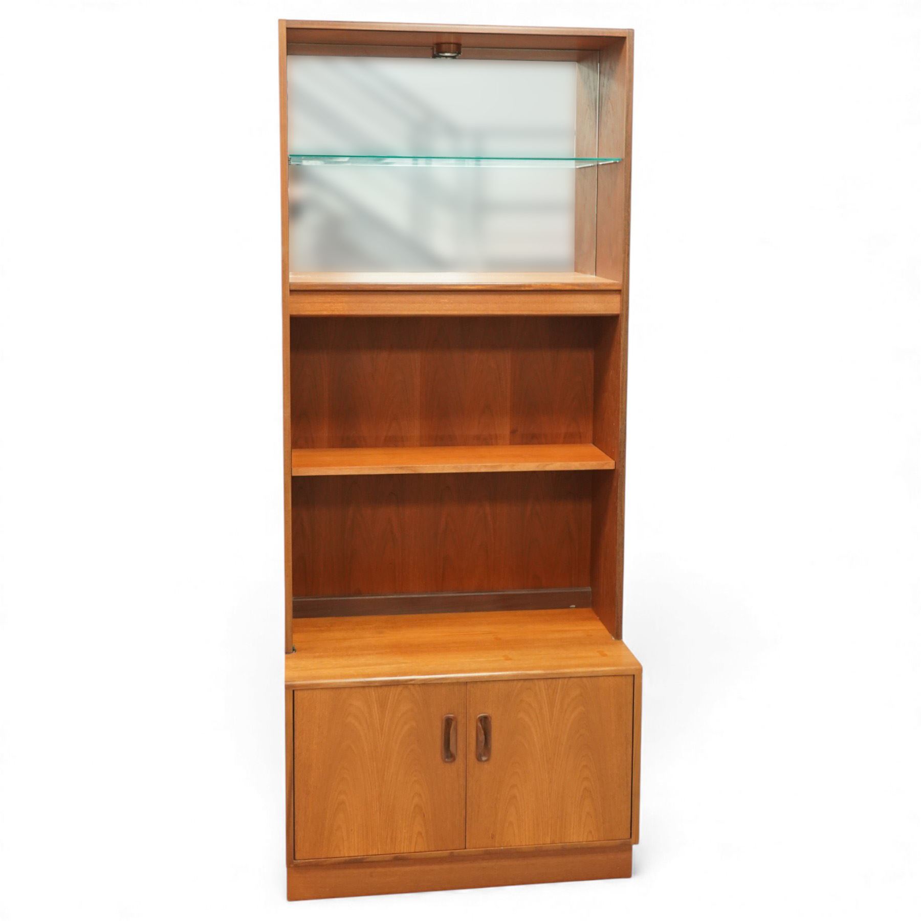 G-Plan - ‘Fresco’ teak bookcase cabinet, rectangular open bookcase with mirrored back panel to the upper section, fitted with a single glass display shelf and two wooden shelves below, the base enclosed by a pair of cupboard doors with shaped teak handles, on a plinth base