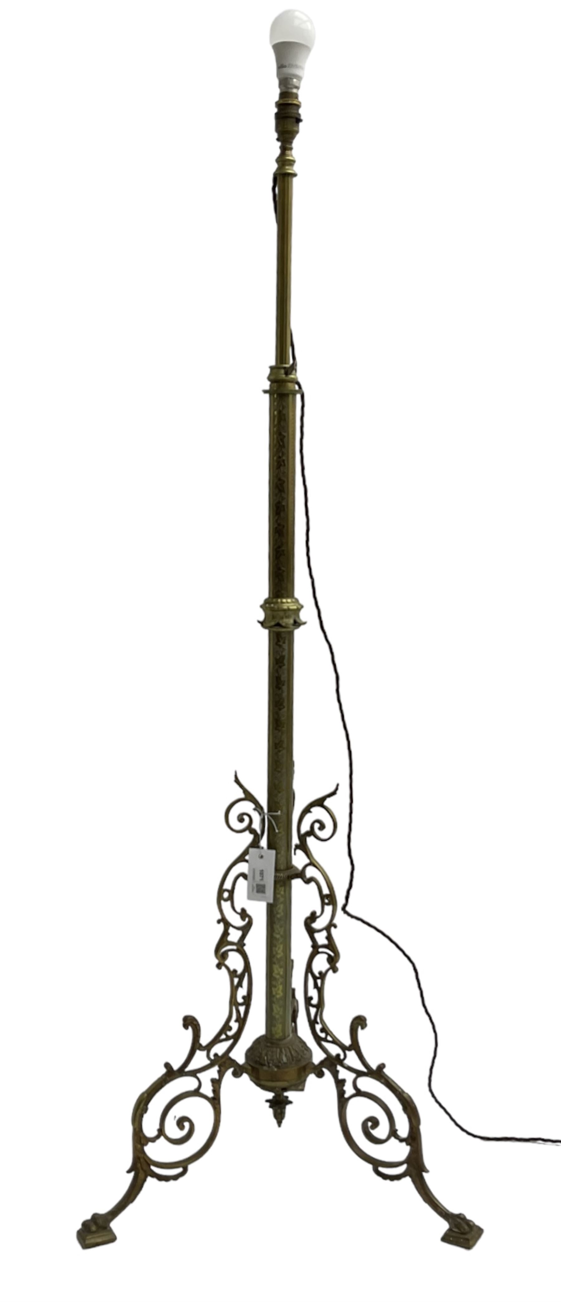 Victorian brass floor standing oil lamp, column decorated with ivy and acanthus leaves, the tripod base pierced with scrolled foliate decoration, with ivory and gilt shade, later converted to electricity