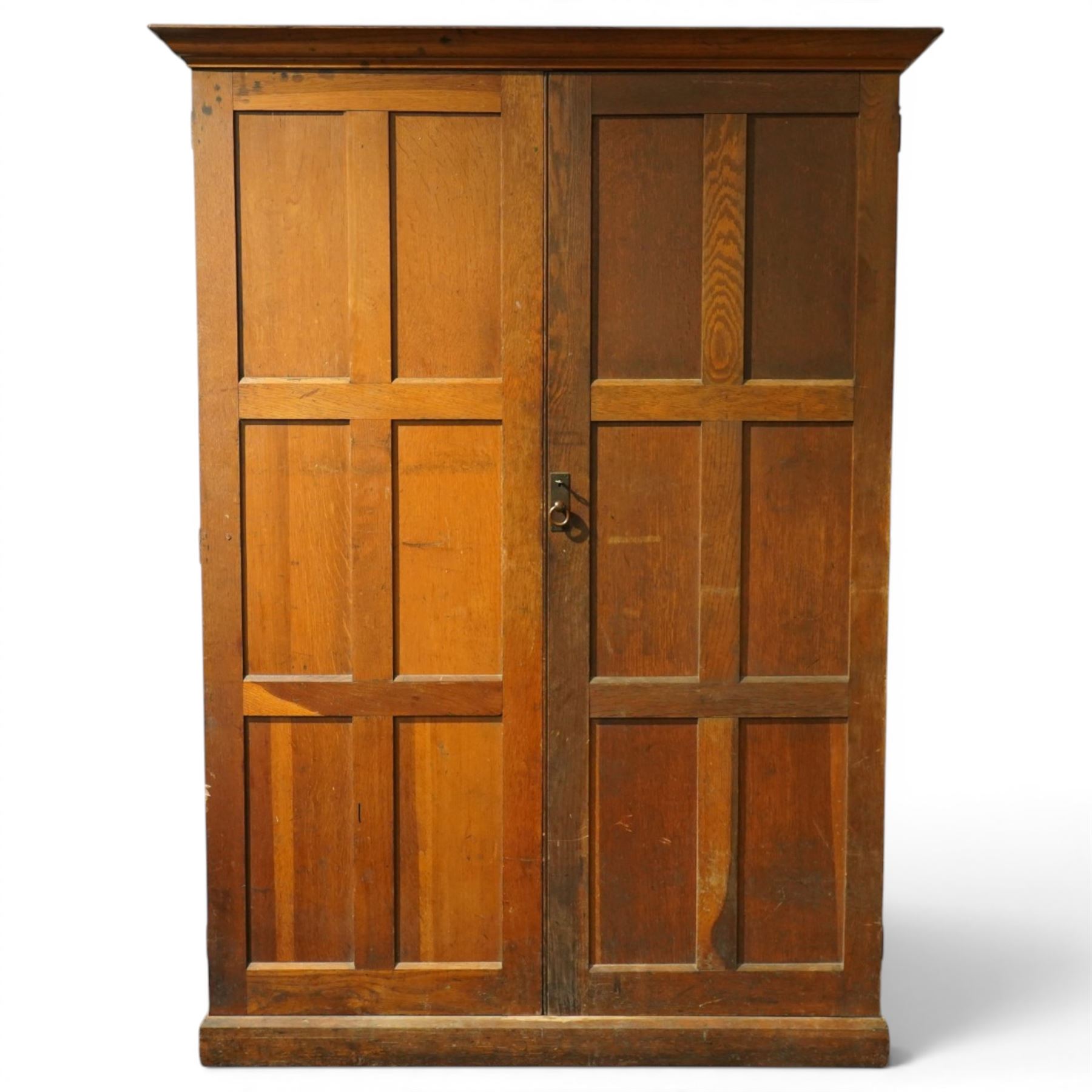 Early 20th century Arts and Crafts oak housekeeper’s cupboard, moulded cornice above pair of panelled doors enclosing a shelved interior, on plinth base