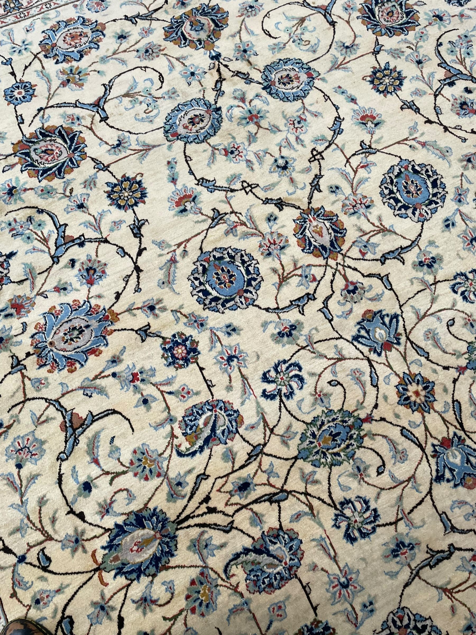 Persian Kashan ivory ground carpet, the field decorated with swirling foliate patterns and stylised plant motifs, scrolling border decorated with palmettes, within floral pattern guard stripes 