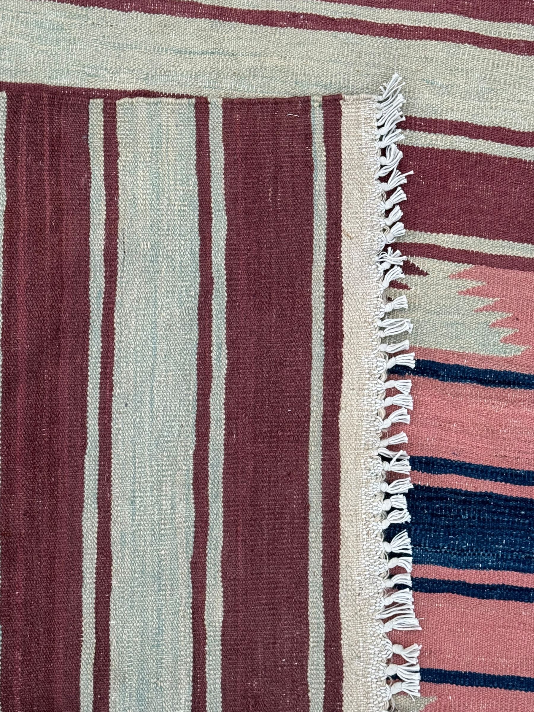 Kilim muted pink ground runner, decorated with rows of horizontal bands in muted tones, alternating with geometric triangular patterns along each band, fringed ends