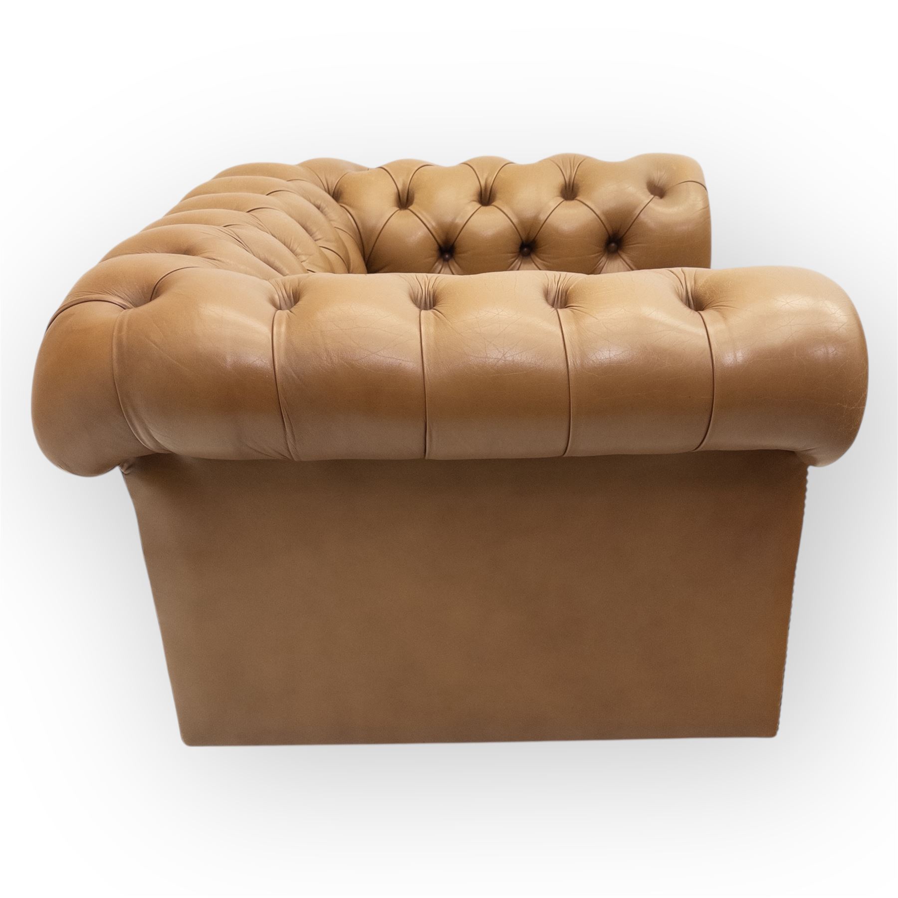 Contemporary set of two tan leather armchairs, comprising a deep-buttoned chesterfield and a matching wingback chair, both with rolled arms, studded borders